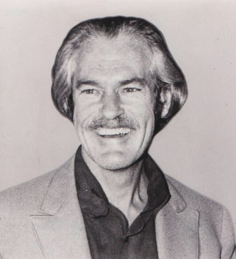 Portrétní fotografie Timothyho Learyho zachycuje jeho usměvavý obličej, obrácený směrem k divákům a mírně doprava. Na sobě má černou košili a šedé sako. Fotografie je v černobílém provedení, což dodává klasický a kontrastní vzhled.